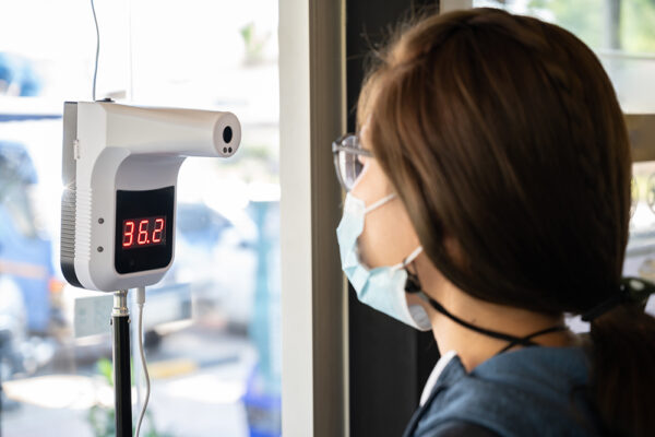 買い物街に入る前に、自動赤外線温度計で温度を測ろうとする女性。 COVID-19の世界的流行の人を識別するために使用する赤外線温度計。